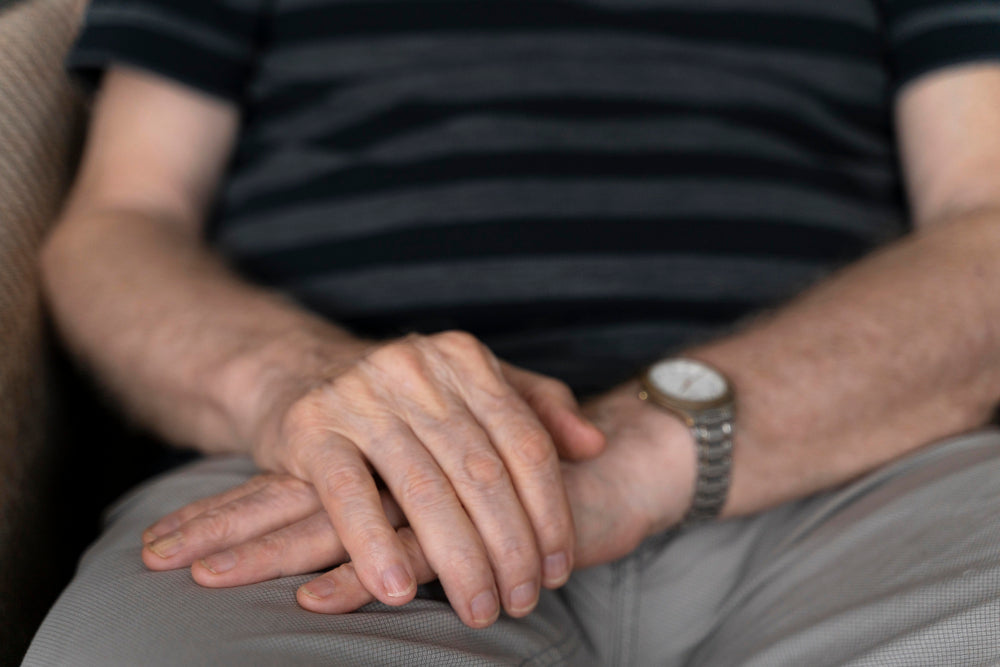 A senior man looking holding his hand, representing a person living with Parkinson’s or a neurological condition