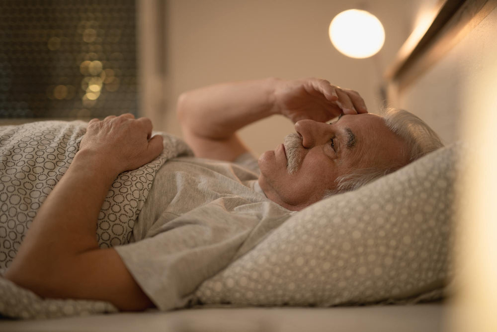 Older adult lying in bed at night, appearing restless, illustrating sleep difficulties commonly experienced with Parkinson’s Disease.