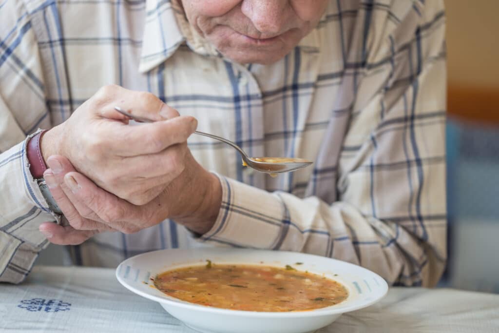 Old man experiencing difficulty eating due to body tremors.