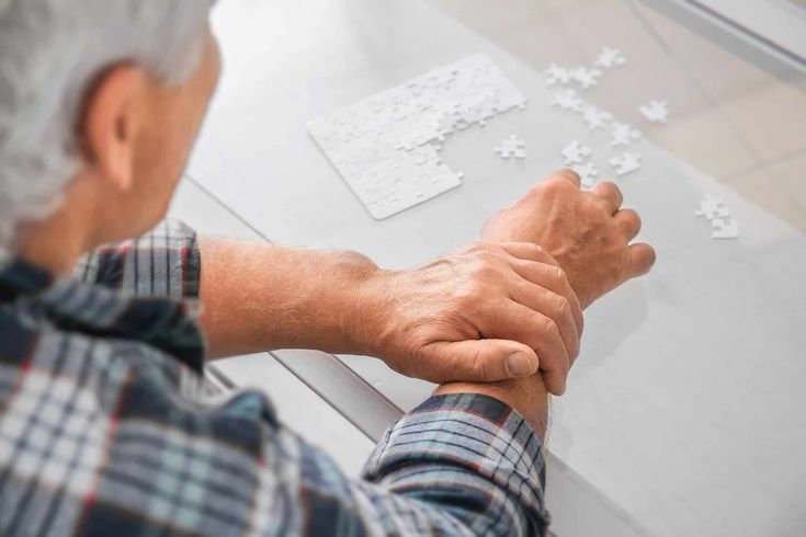 Elderly man tries to complete a puzzle, steadying his trembling hand due to Essential Tremor.