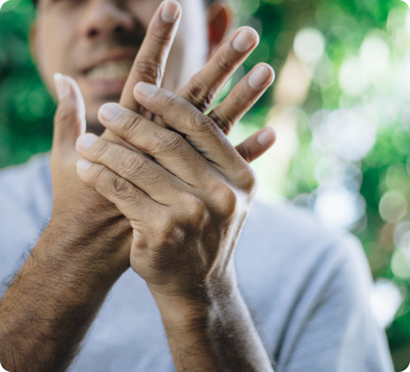 A close-up of a person's hands in pain, holding their elbows, with a blurred green outdoor background.
