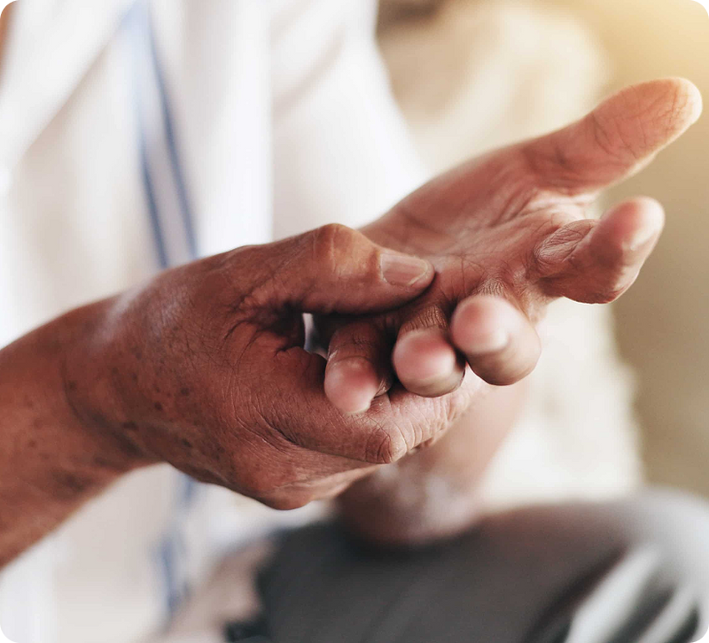 Close-up of an elderly person's hands, with one hand holding the other and showing a small cut or abrasion on the fingers, against a softly blurred light background.