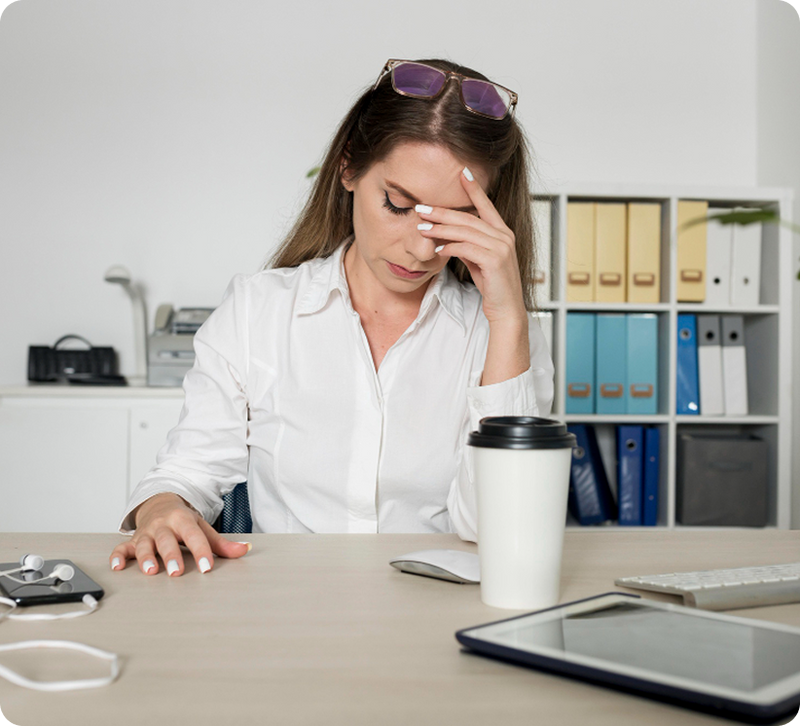 Stressed woman resting her head in her hand at an office desk, representing the emotional and physical fatigue of managing Parkinson's Disease at work.