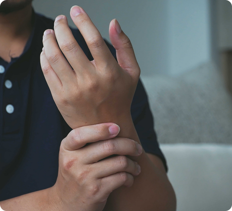 A close-up of a person holding and cramping their wrist, wearing a dark navy blue polo shirt in a softly lit indoor setting.