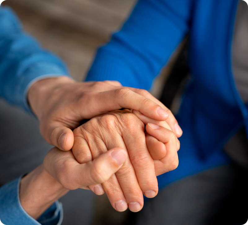 Younger person gently cradling the hands of an older adult, representing caregiver support for someone living with Parkinson's Disease.