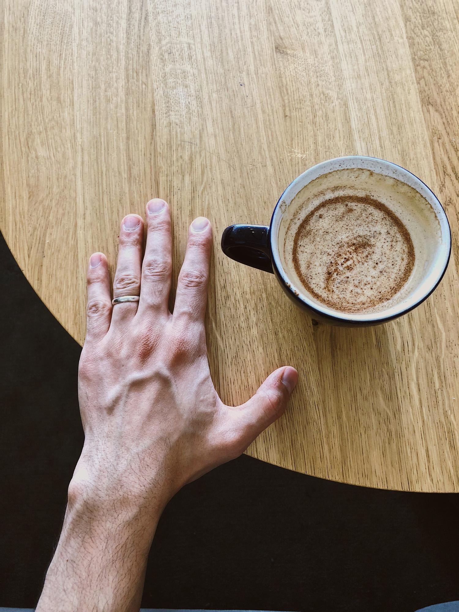 Hand resting flat on a wooden table beside a coffee cup.