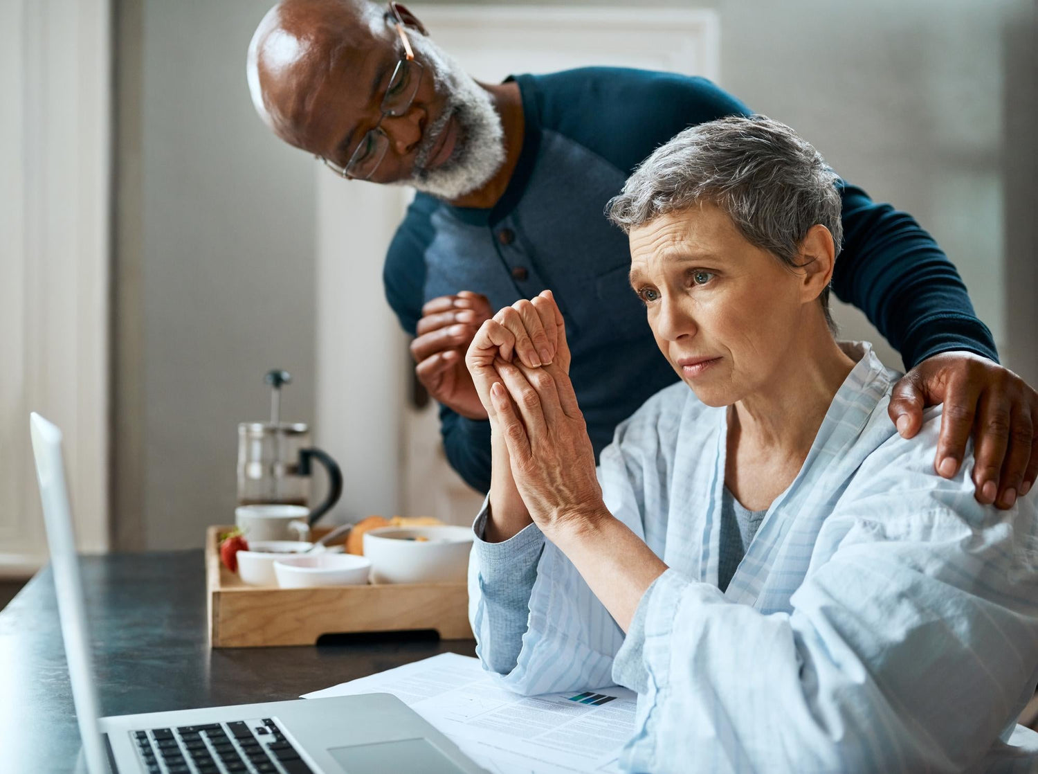 An older woman showing signs of Essential Tremor isolation while a caregiver offers support indoors.