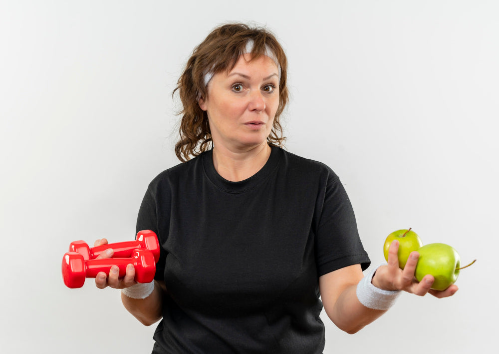 Middle-aged woman holding apples and dumbbells, symbolizing the role of diet and exercise in managing and preventing Parkinson’s disease.