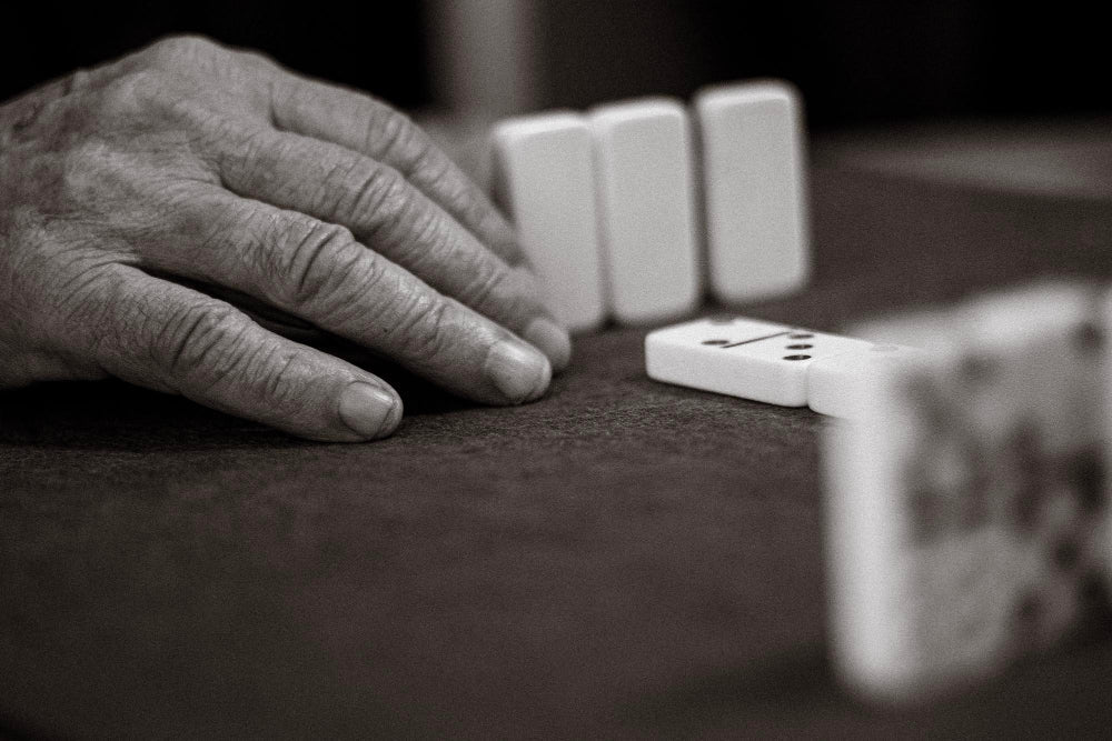 Parkinson's stage 2, with an elderly person's hands with visible veins, playing dominoes.