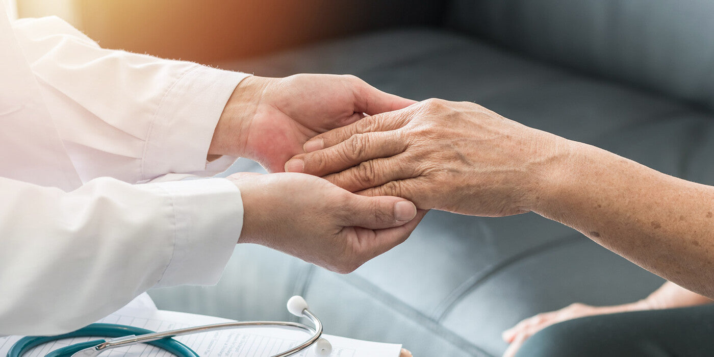 Close-up of doctor's hands holding elderly patient's hand.