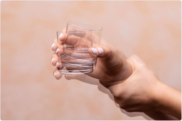 A hand holding a glass that appears shaky, illustrating the sensation of internal vibrations when lying down and a body feels shaky inside.