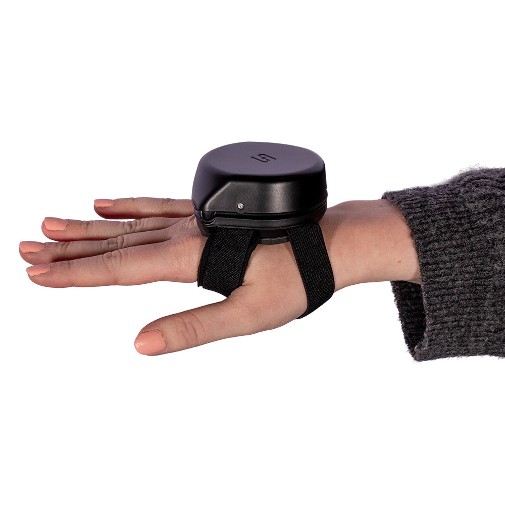 Hand wearing the Steadi-3 anti-tremor device on the back of the hand, secured with a black strap, against a clean white background.