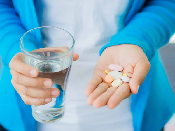 Woman holding essential tremor medication pills with a glass of water.