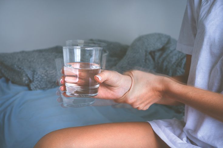 A person holding a glass of water with a shaky hand, representing the struggles of famous people with essential tremor and raising questions like does Bill Clinton have Parkinson's.
