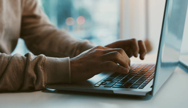 Person typing on a laptop keyboard at a desk, close-up of hands working on a computer for remote work, coding, or online business tasks.