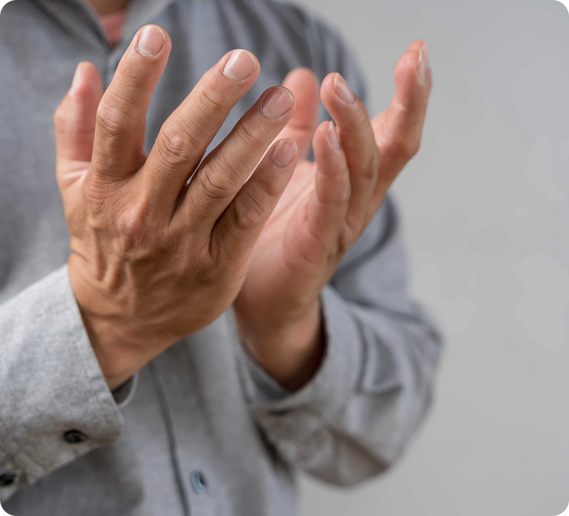Close-up of a person's hands in front of their face, wearing a light gray long-sleeve button-up shirt against a soft gray background.