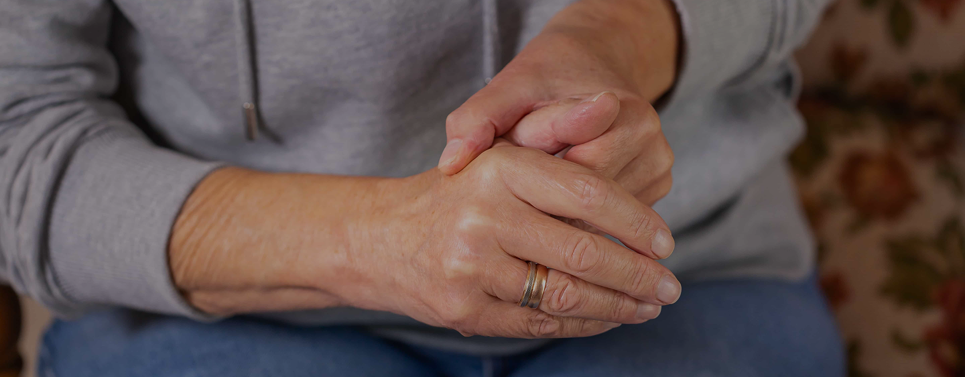 Person with a wedding ring clasping their own hands in their lap, representing the daily challenges of living with Parkinson's Disease at work.
