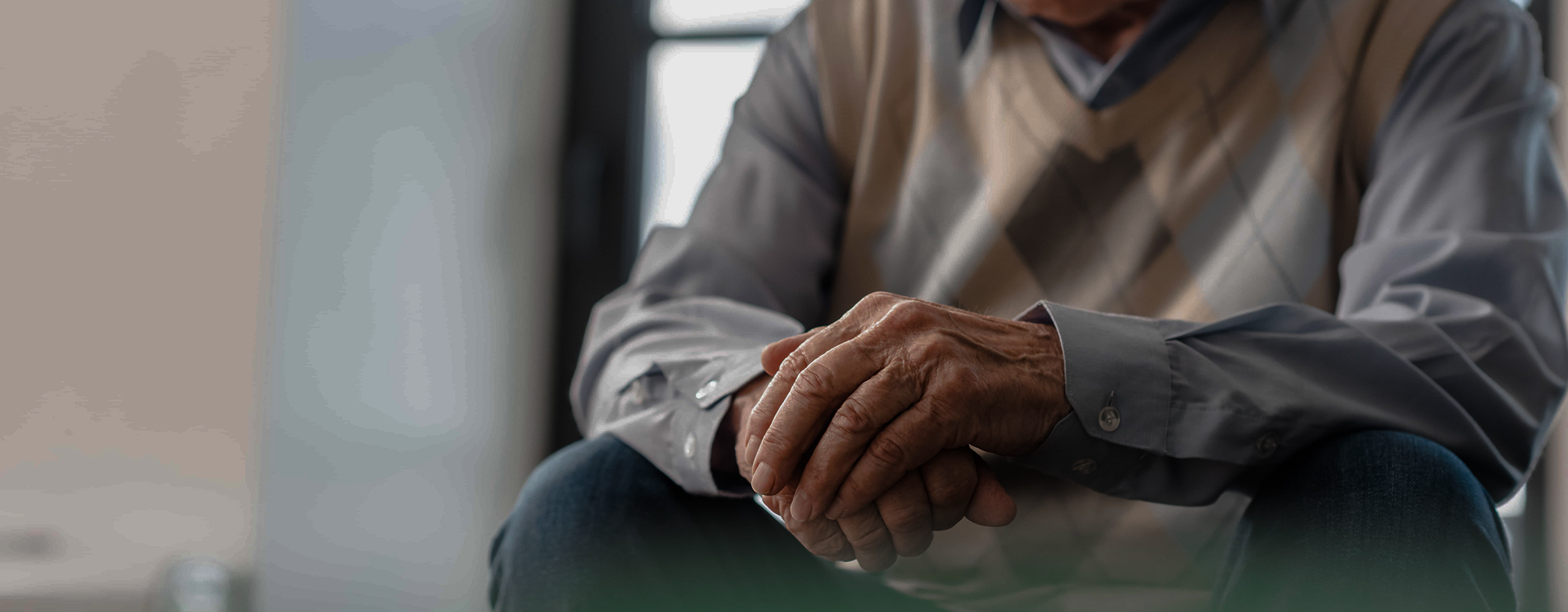 Early signs of Parkinson's Disease, where a senior man's hands show finger and wrist pain at home.