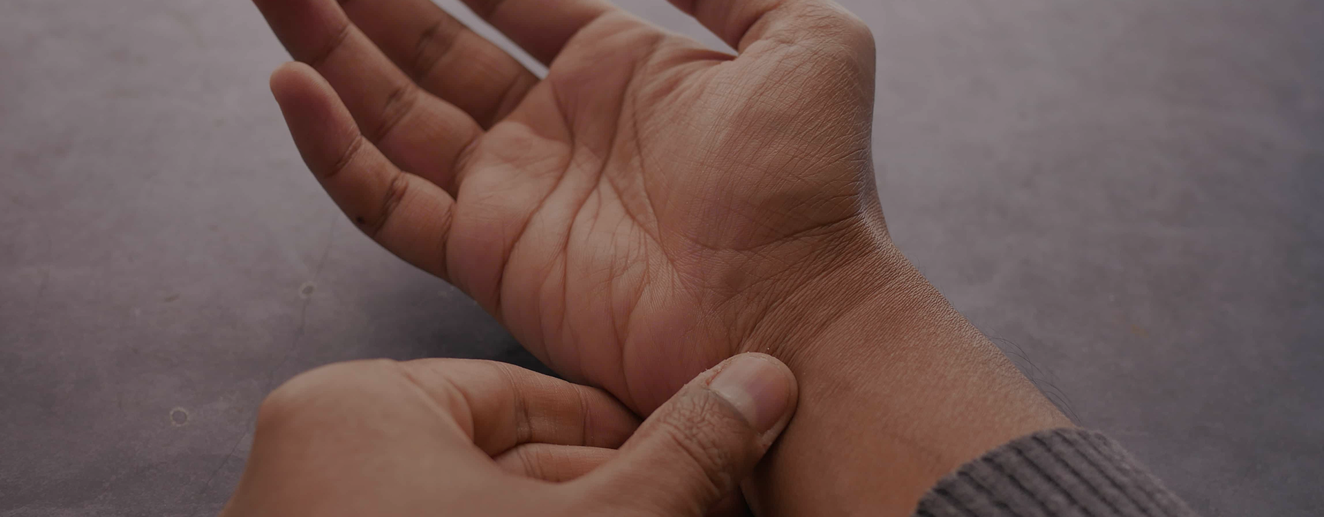 A close-up of a person's wrist and hand being held by another hand, with the skin of the wrist and forearm shown against a plain gray background.